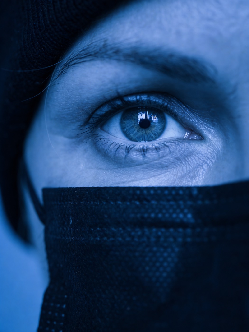 Nahaufnahme eines Auges über einem Mund-Nasen-Schutz in kühlem Blau (KI-generiertes Bild)