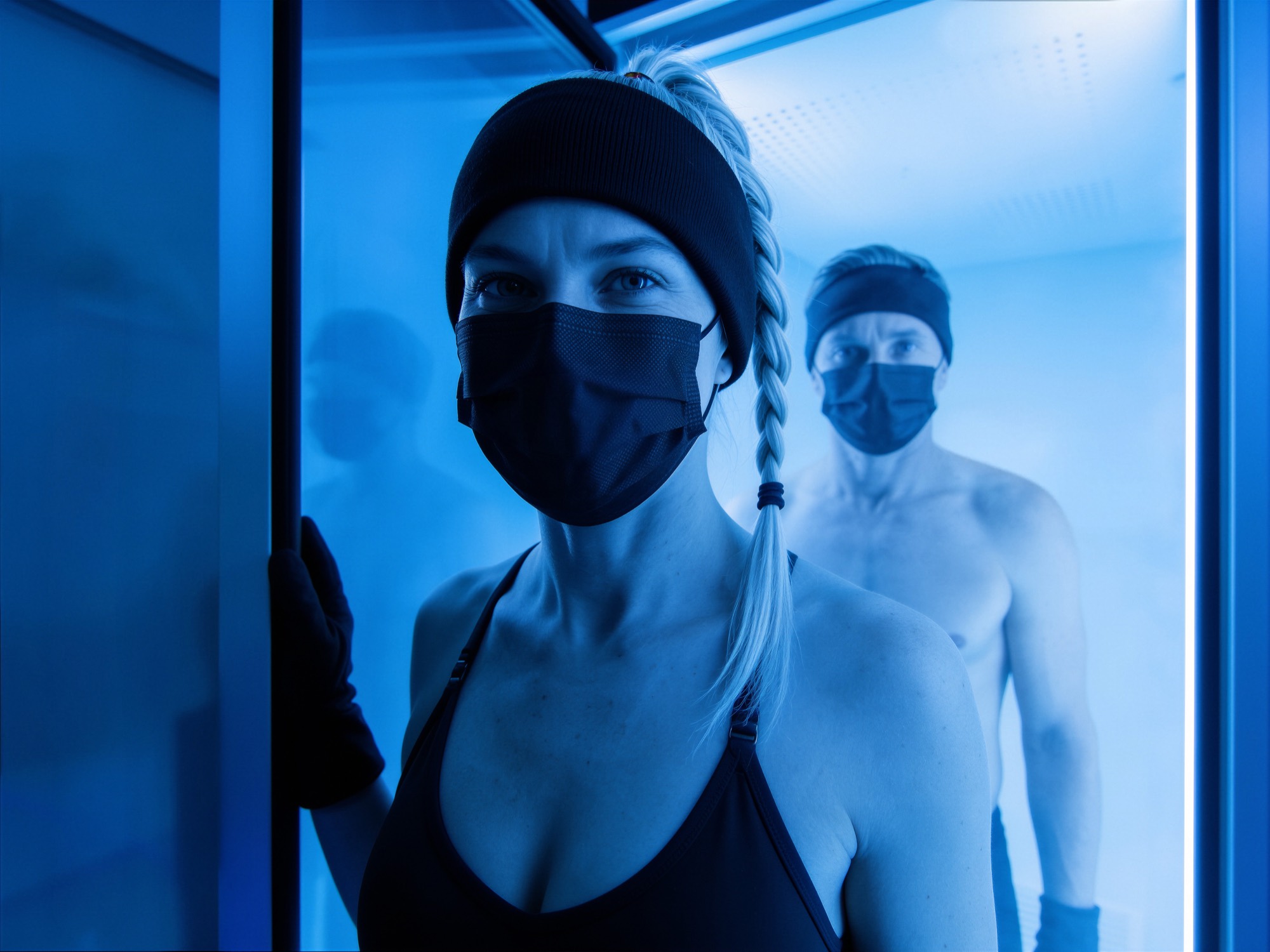 Frau und Mann mit Stirnband, Mund-Nasen-Schutz und Handschuhen in einer Kältekammer (KI-generiertes Bild)
